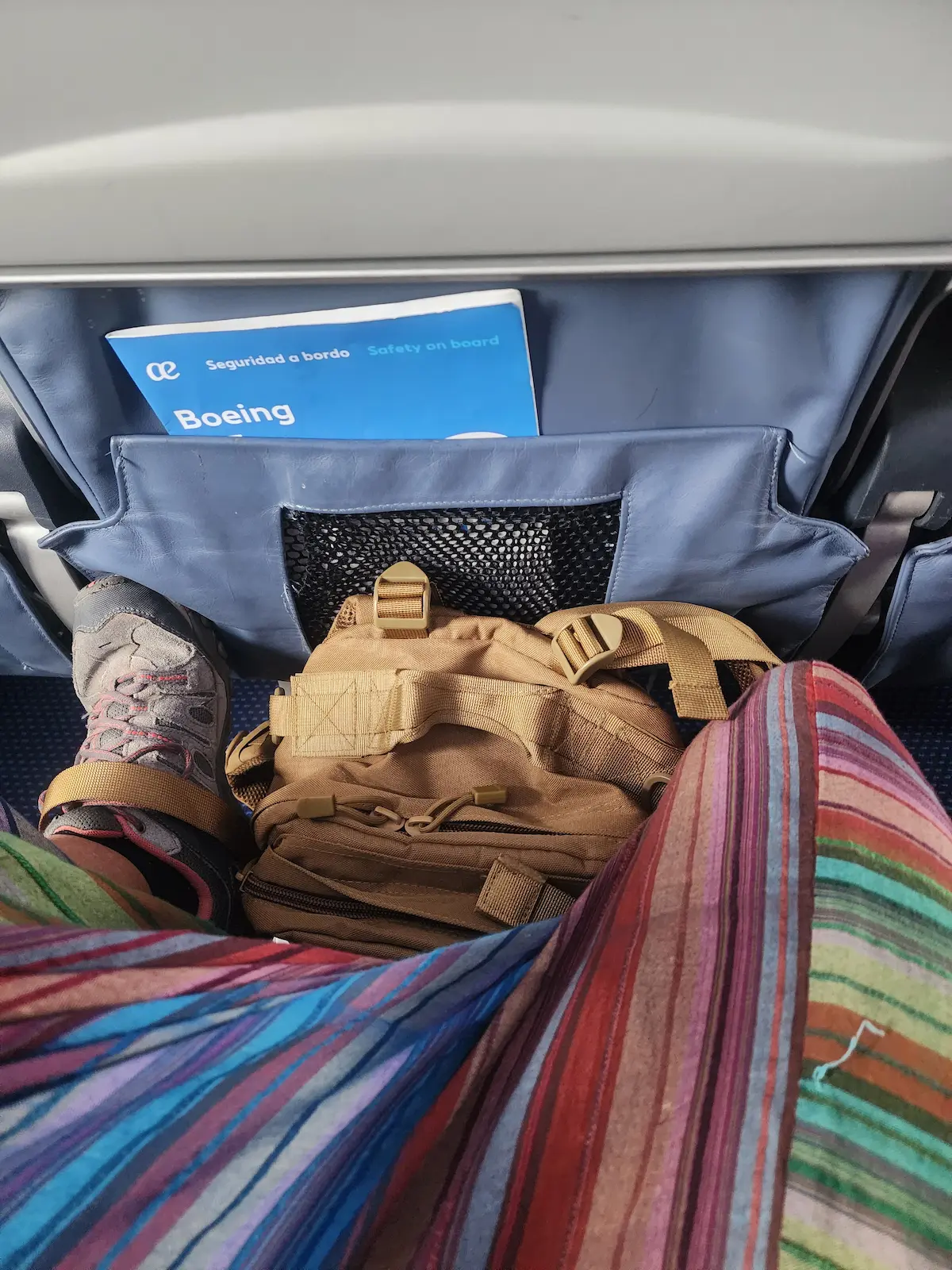Mochila y piernas de una viajera en un avión rumbo a Asia: viajar sin organizar nada empieza antes de despegar