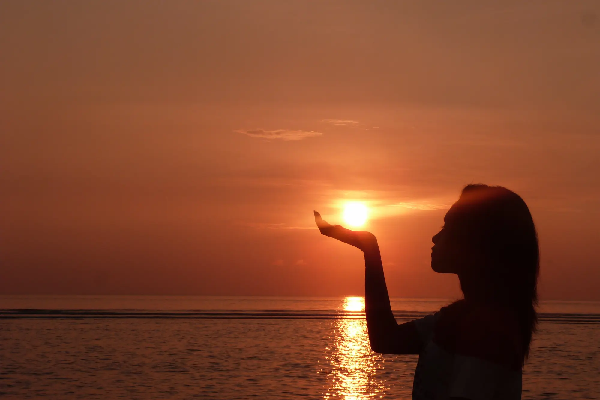 Silueta de una mujer al amanecer en Bali sosteniendo el sol entre las manos, la isla en silencio durante Nyepi