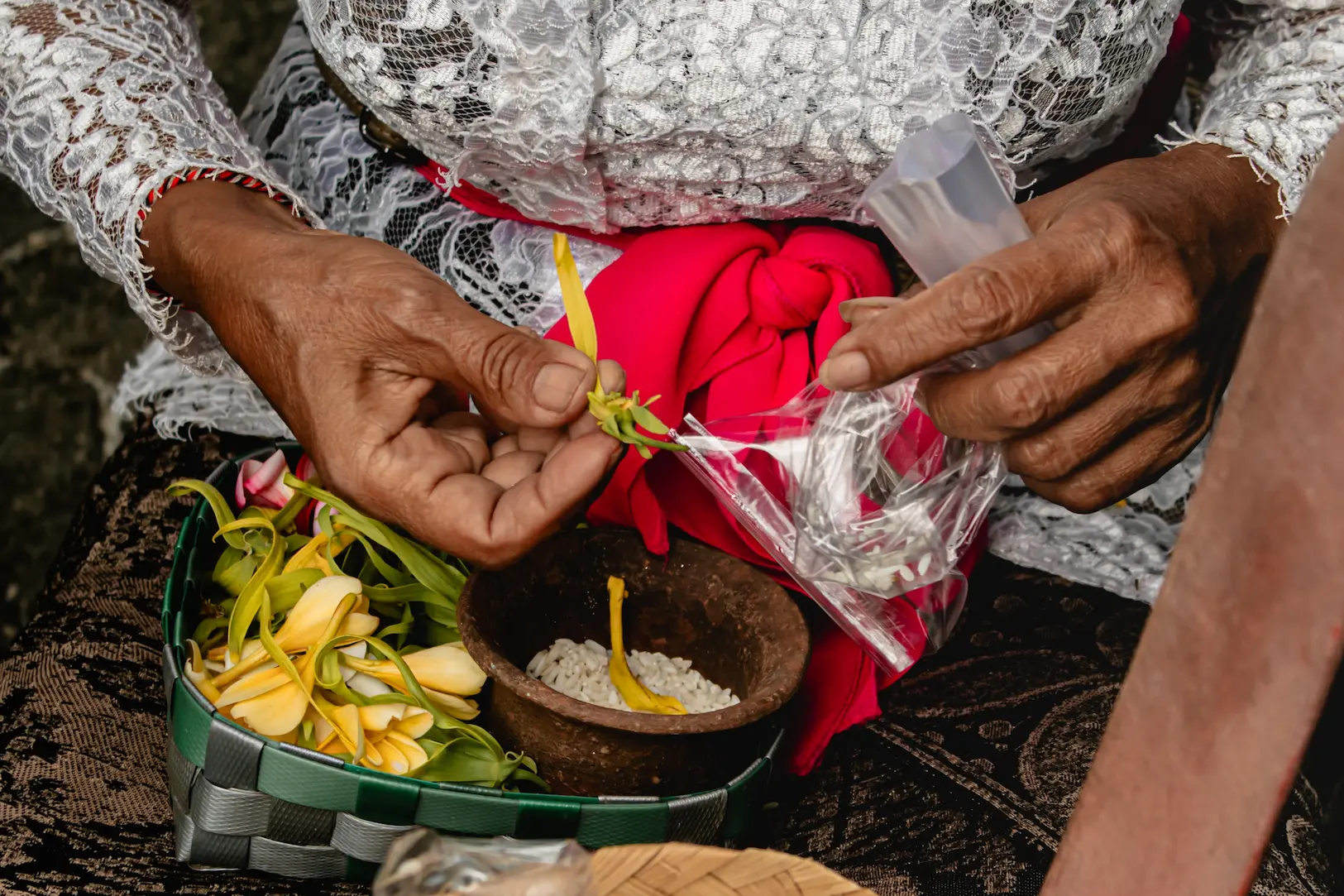 Manos de una mujer preparando un canang sari con flores y arroz