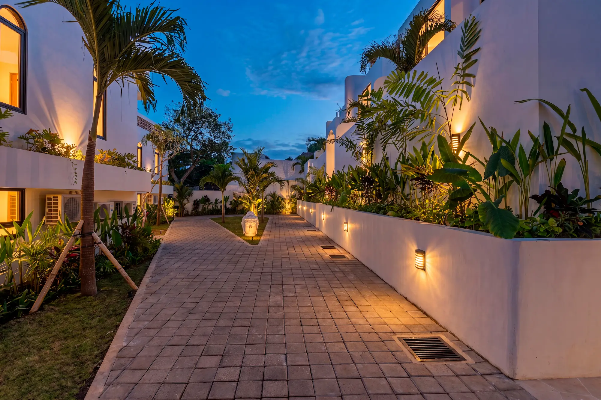 Calle interior del complejo iluminada de noche entre jardines