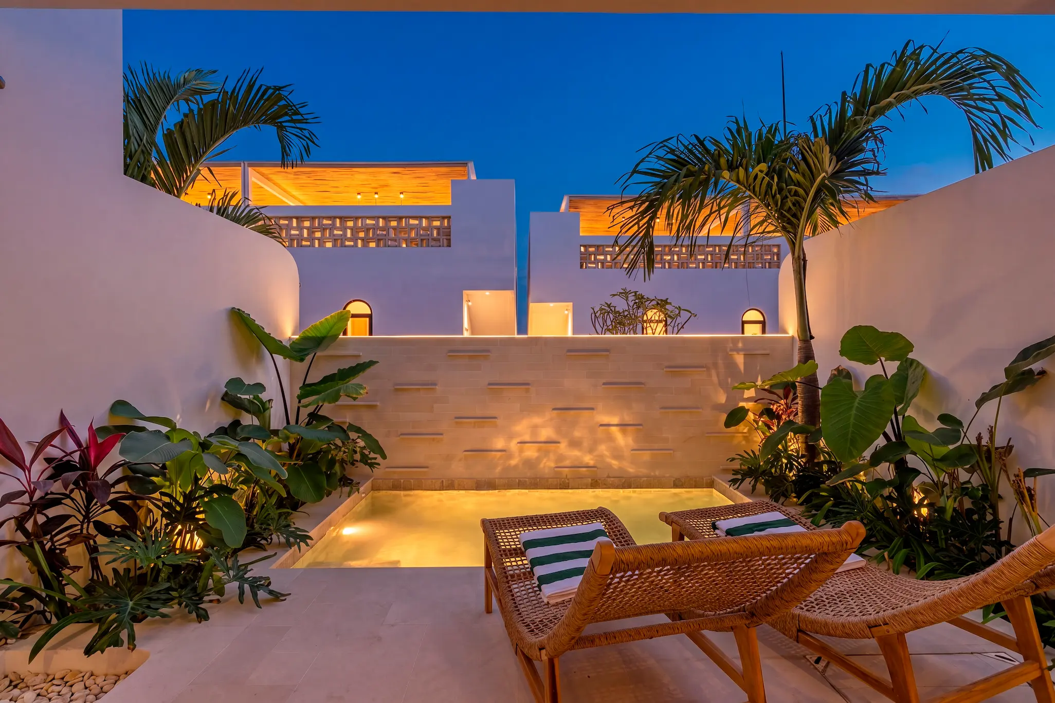 Piscina privada iluminada al anochecer, entre muros blancos y palmeras
