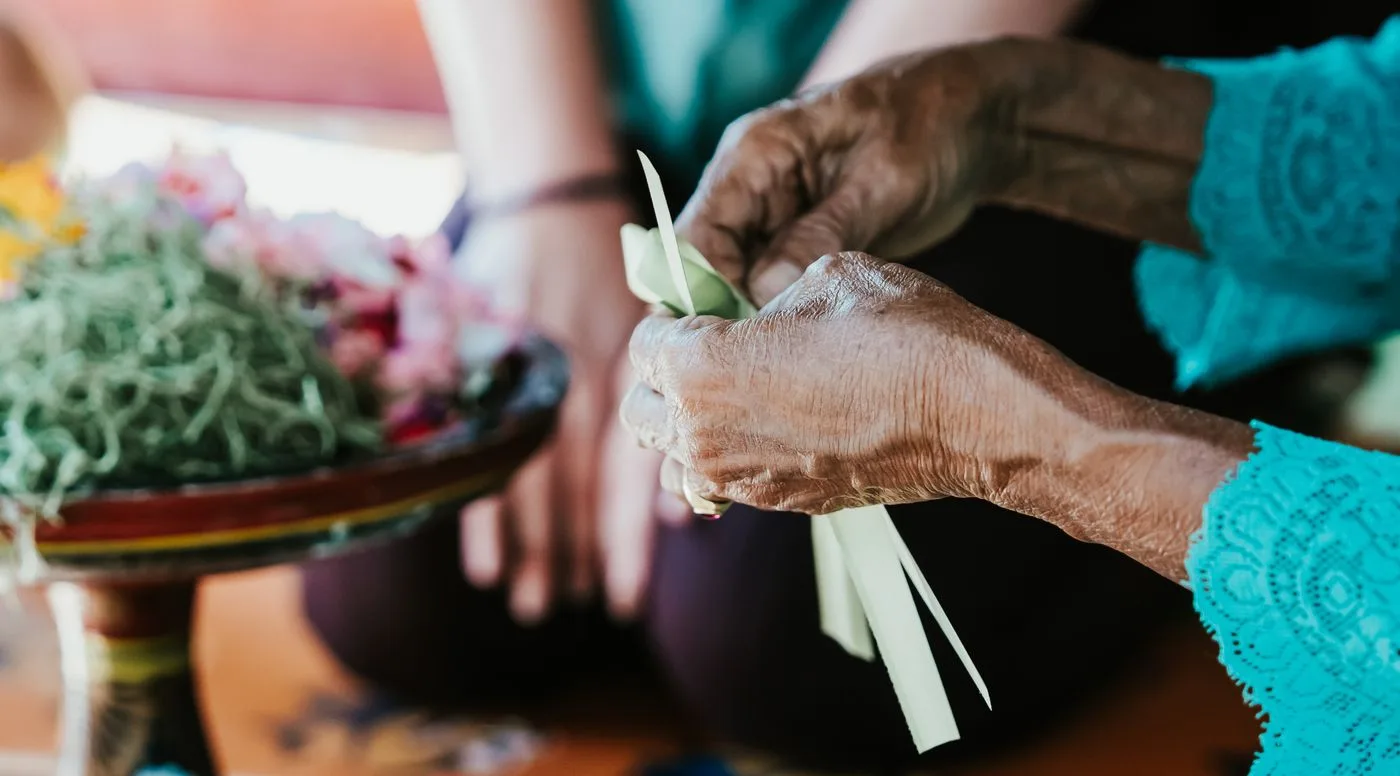 Manos de una mujer balinesa preparando una ofrenda con hojas y flores